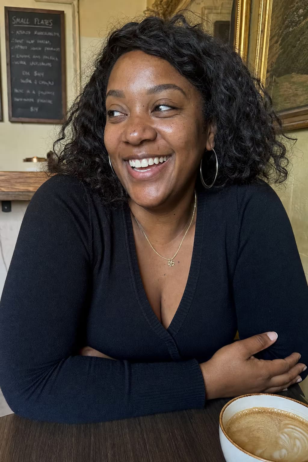 Photo of a woman with wavy hair smiling over a coffee in a cozy café — the photo a customer uploaded.